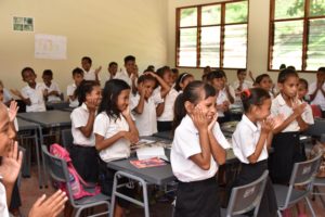 Classroom in Timor-Leste, Primary school children standing and clapping, holding face