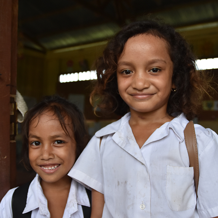 Two school girls from Timor Leste in door frame of school classroom smiling at camera.
