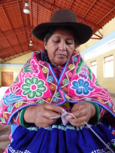 Peruvian Woman in traditonal dress knitting wearing brown hat looking down at her hands