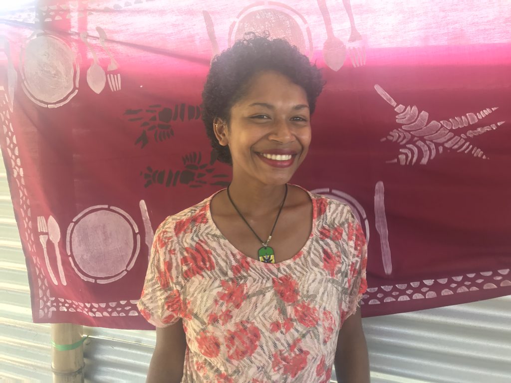 Young Fijian woman smilling at the camera standing in front of traditional material.